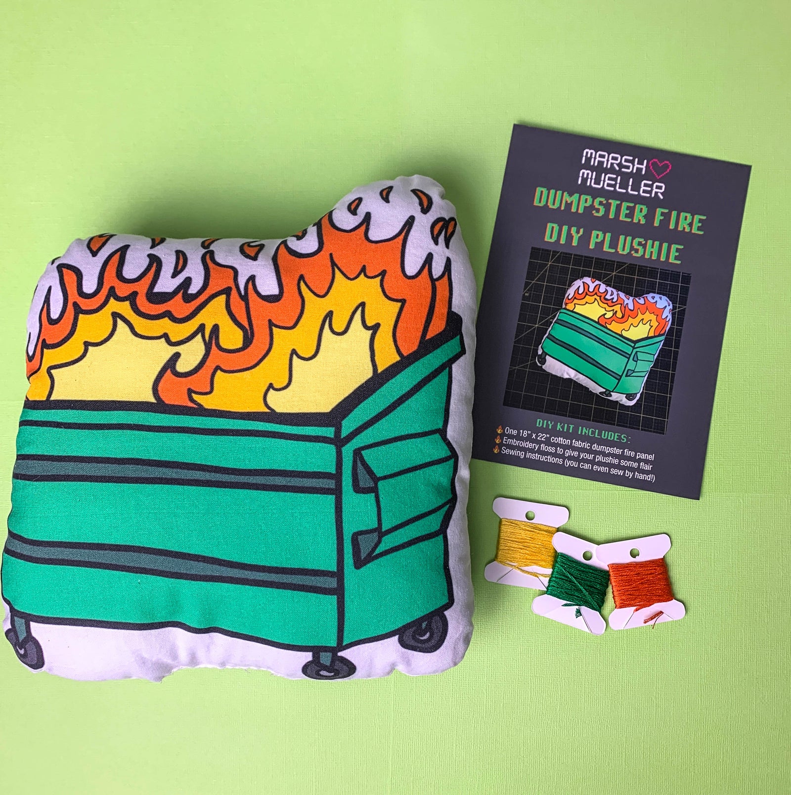 Flatlay of dumpster fire plushie next to packaging card and embroidery floss. All part of the Dumpster Fire DIY Plushie Kit