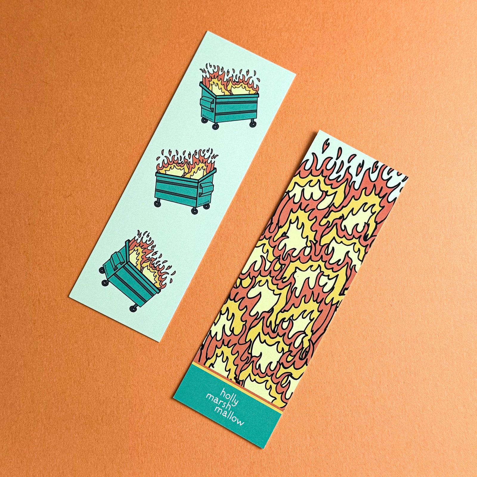 A colorful bookmark with an illustration of a dumpster on fire, with flames in shades of red, yellow, and orange, on an orange background.