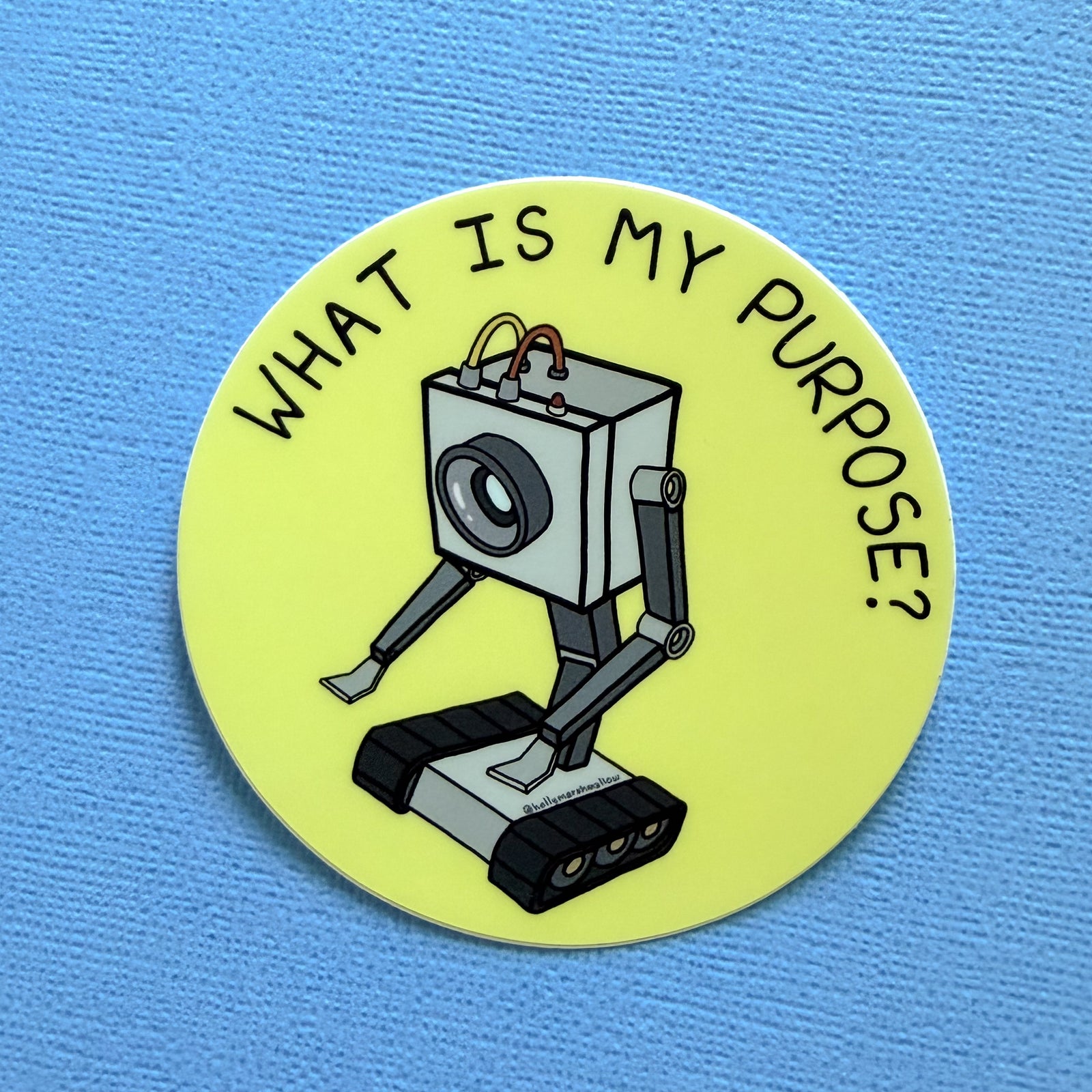 Yellow circle sticker with the Butter Robot from Rick + Morty in the center with hand-lettered text that reads What is My Purpose? on a blue background
