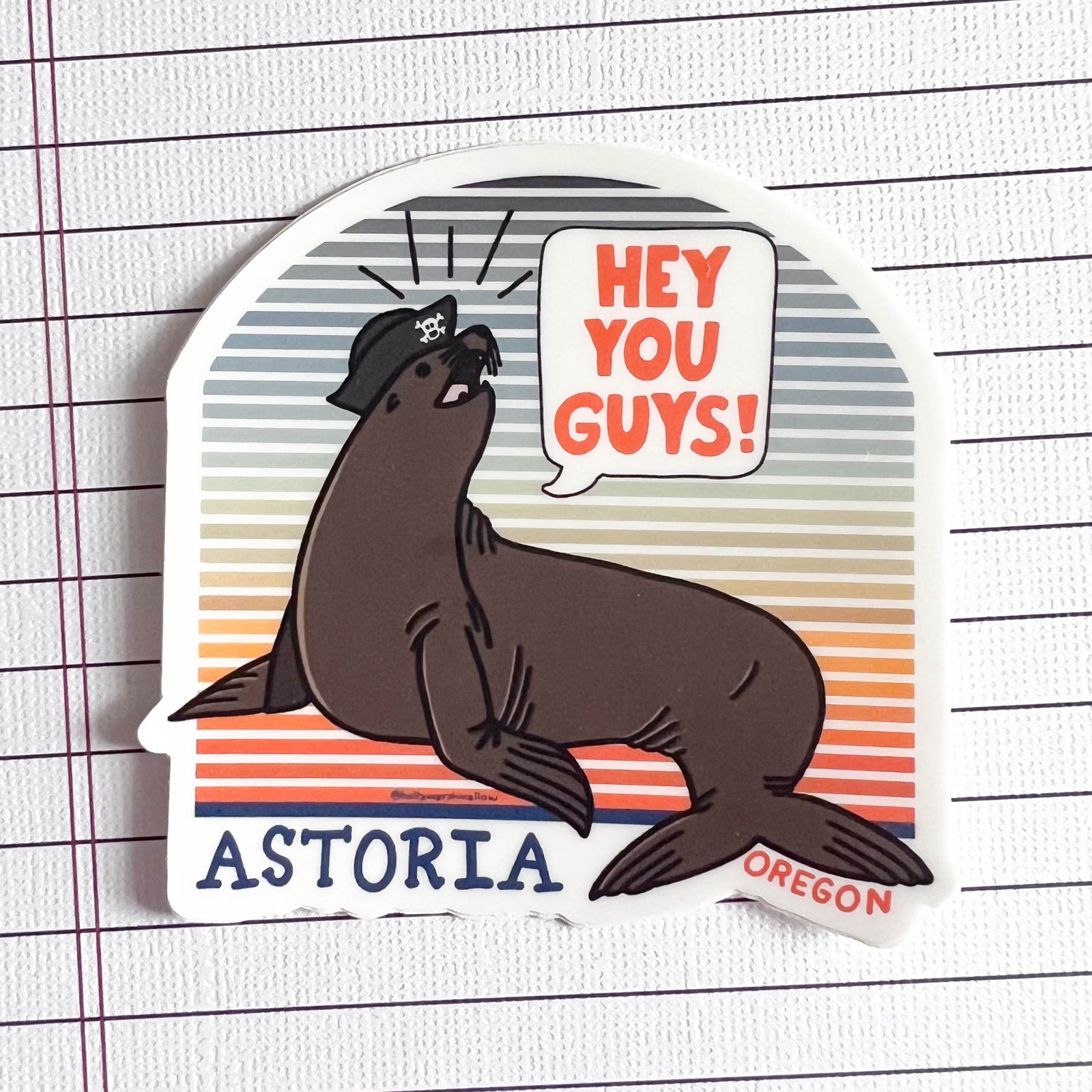 Sticker of a seal with a speech bubble saying 'Hey You Guys!' and text 'Astoria Oregon' on a striped background.