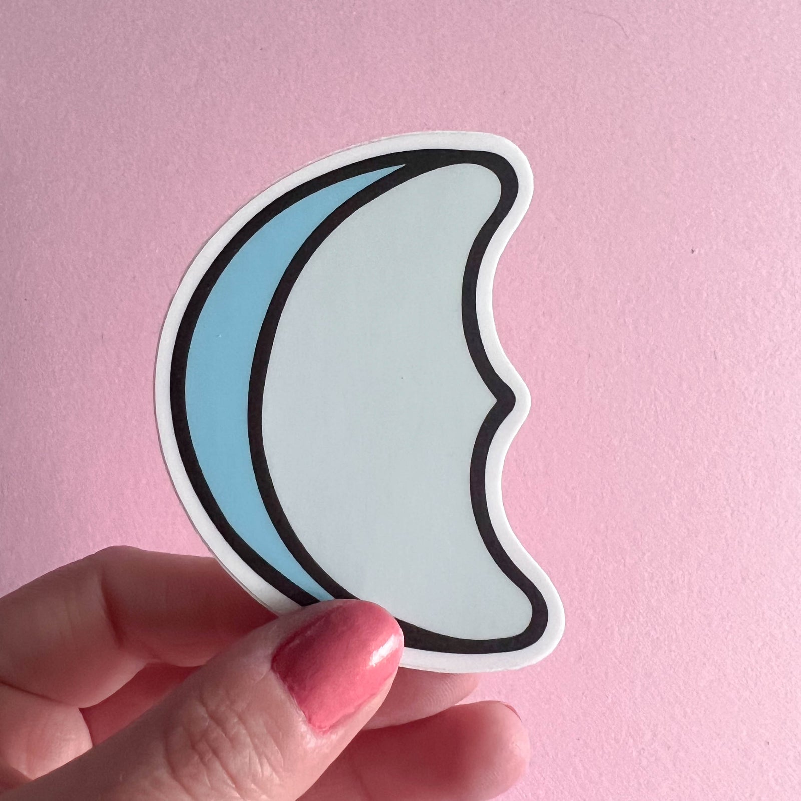 Hand holding a crescent moon-shaped sticker on a pink background