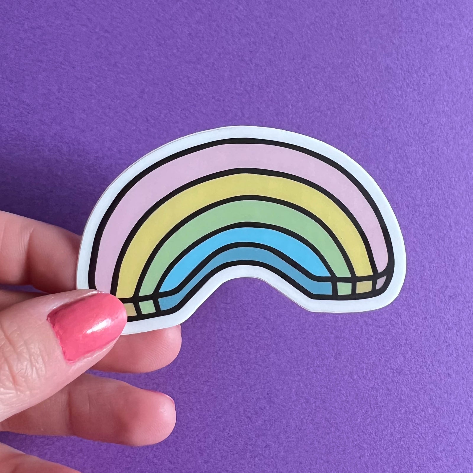 Hand holding a rainbow sticker against a purple background