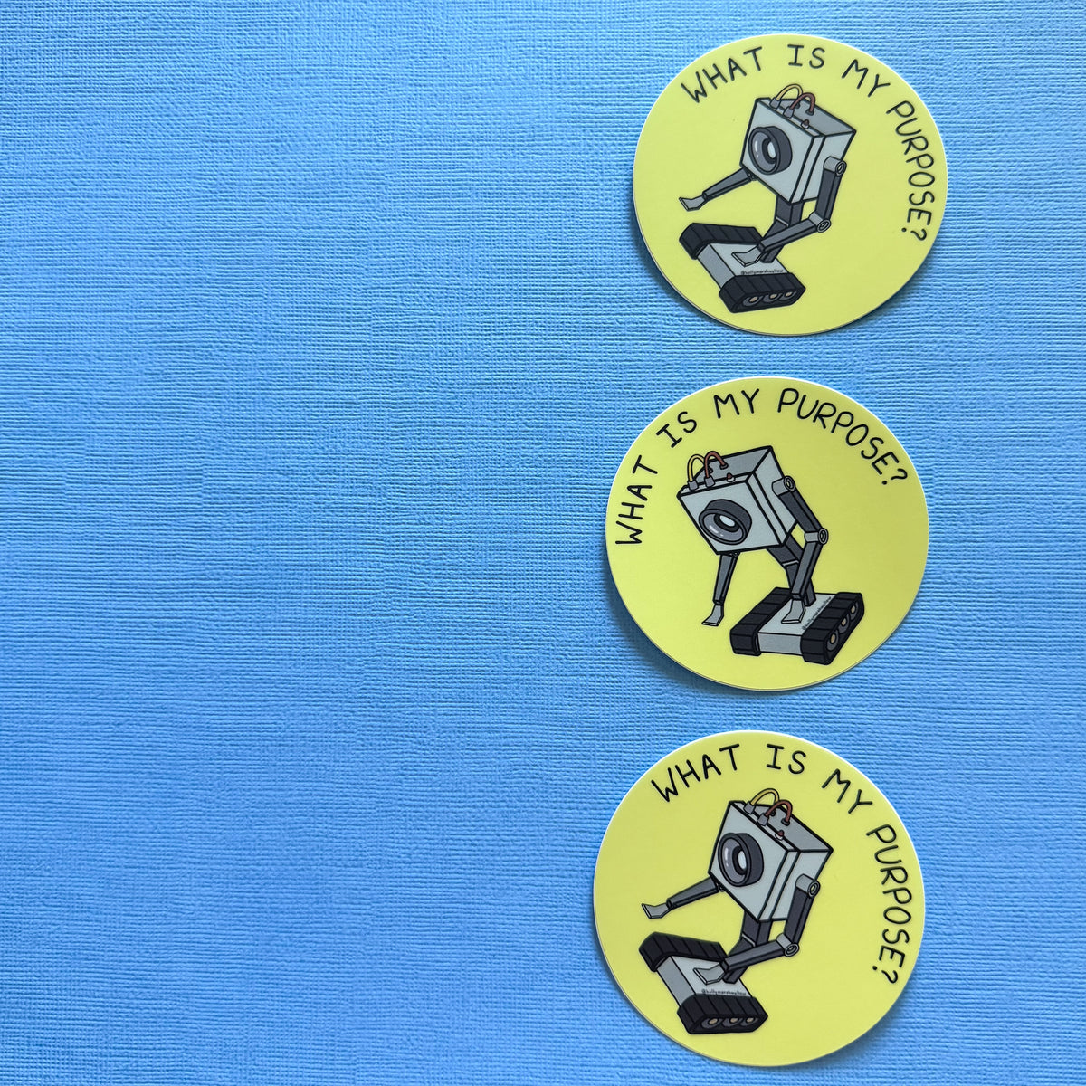 Three Yellow circle stickers with the Butter Robot from Rick + Morty in the center with hand-lettered text that reads What is My Purpose? on a blue background
