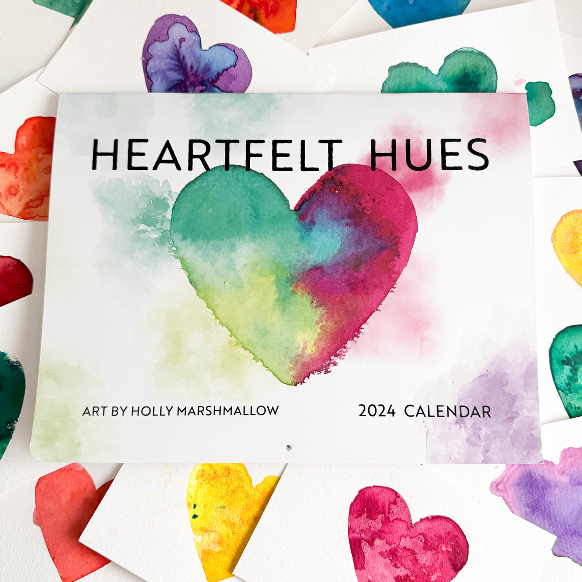 flatlay of calendar with small watercolor heart paintings laid underneath as the background