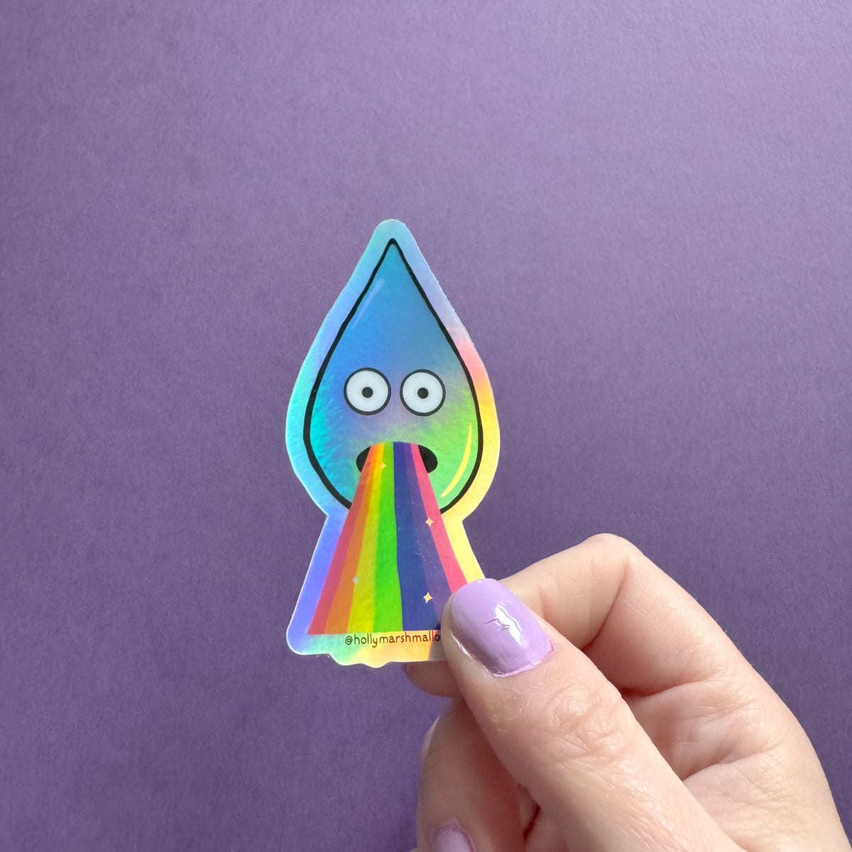 Hand holding a colorful sticker of a droplet with rainbow barf against a purple background
