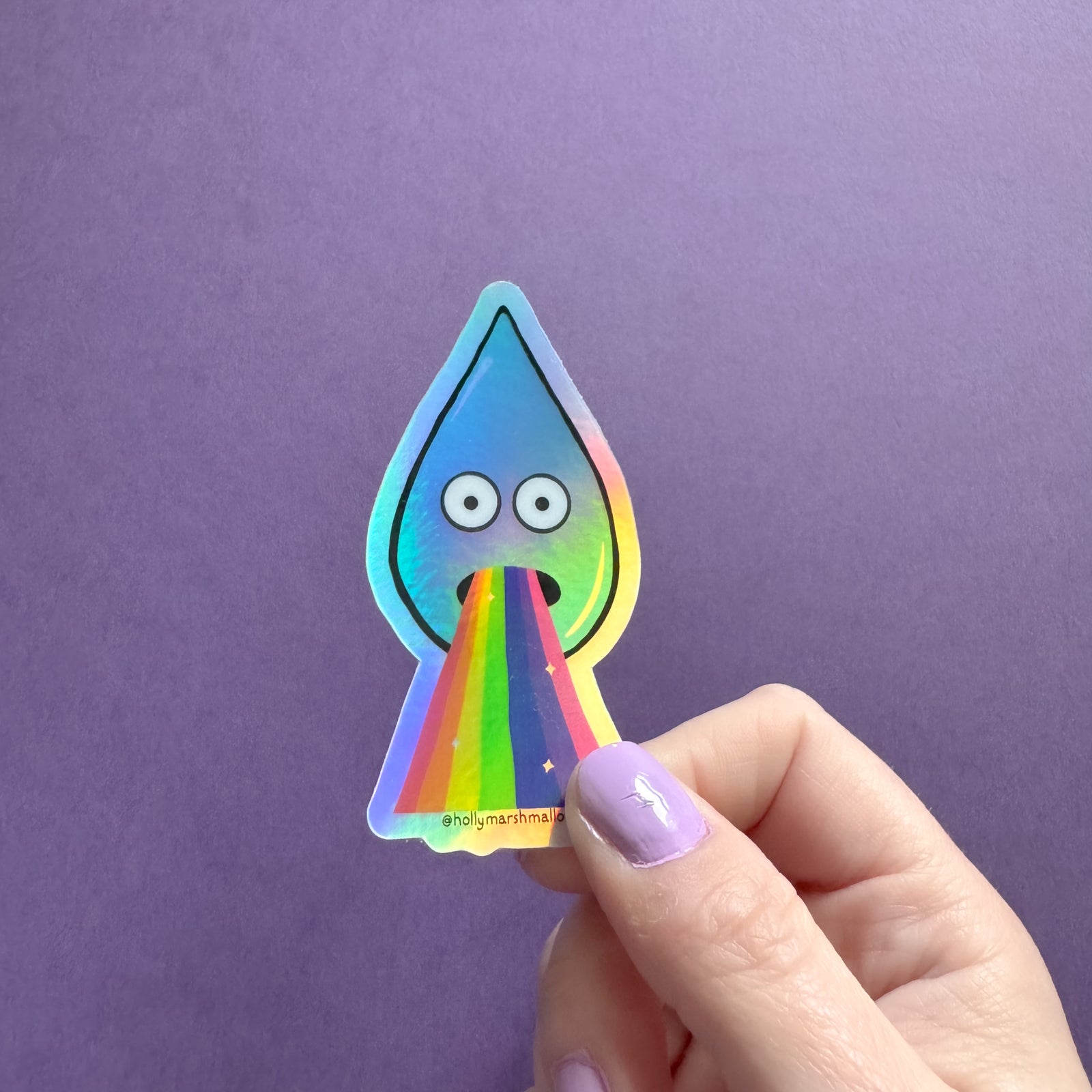 Hand holding a colorful sticker of a droplet with rainbow barf against a purple background