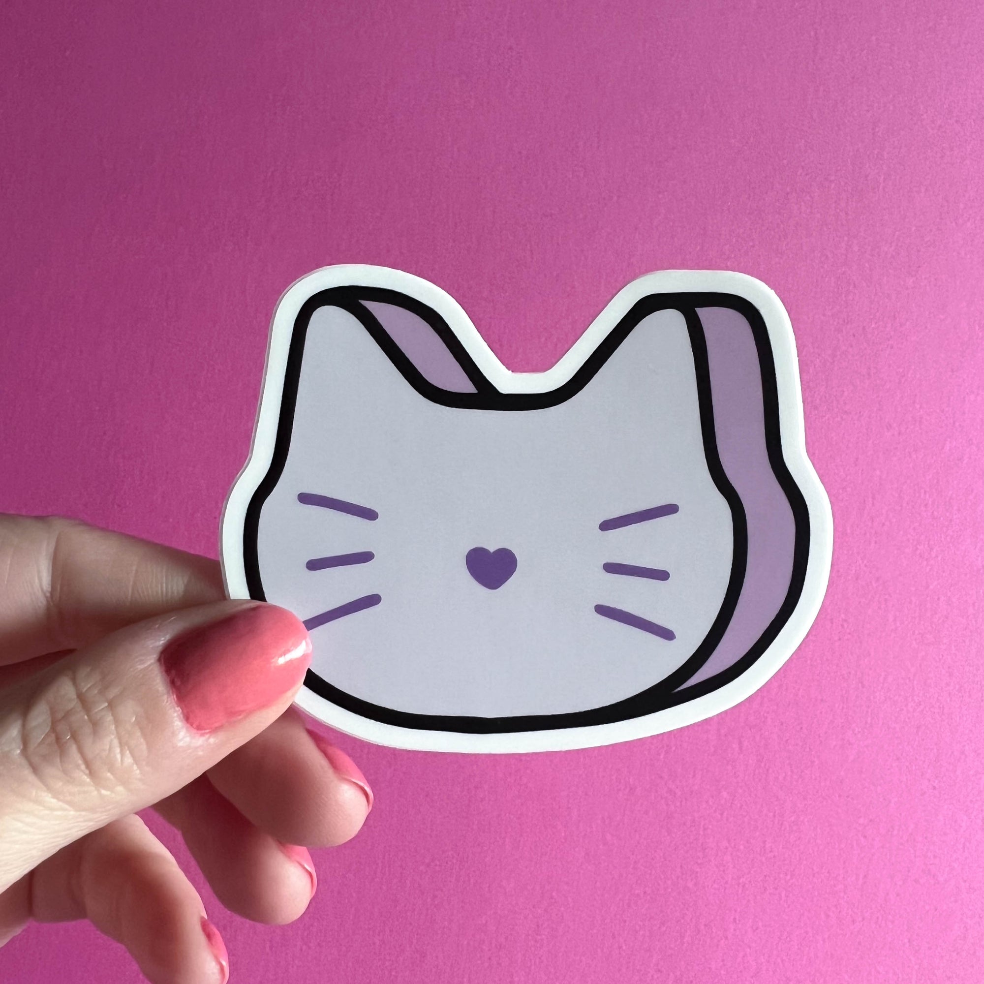 Hand holding a sticker of a marshmallow cat face on a pink background