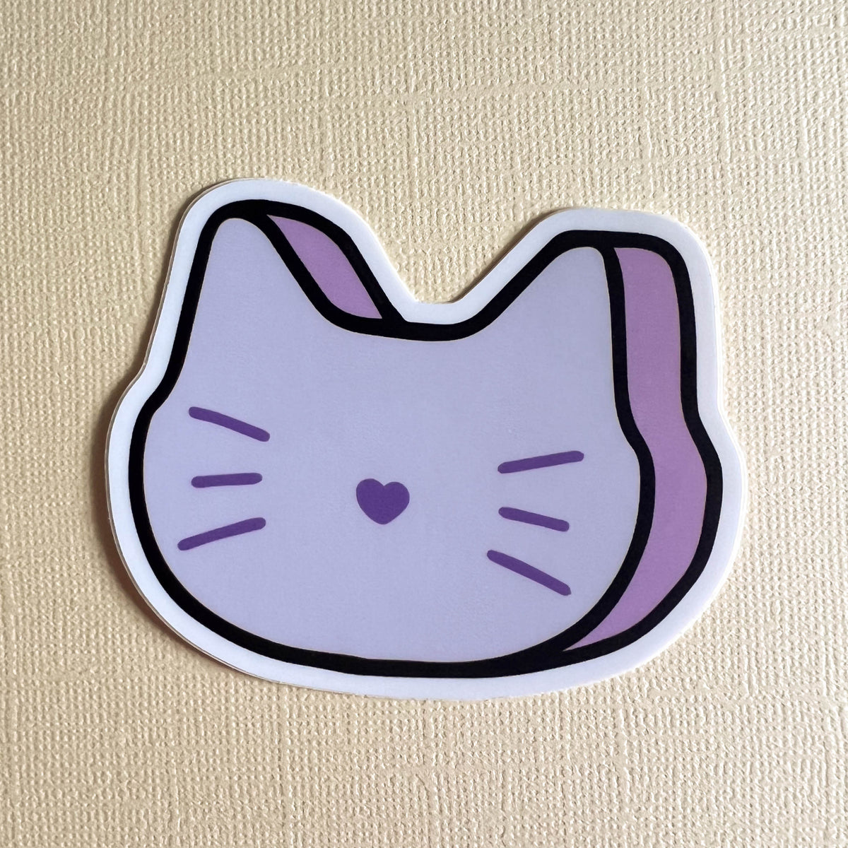 Sticker of a marshmallow cat face with a purple heart on a yellow background