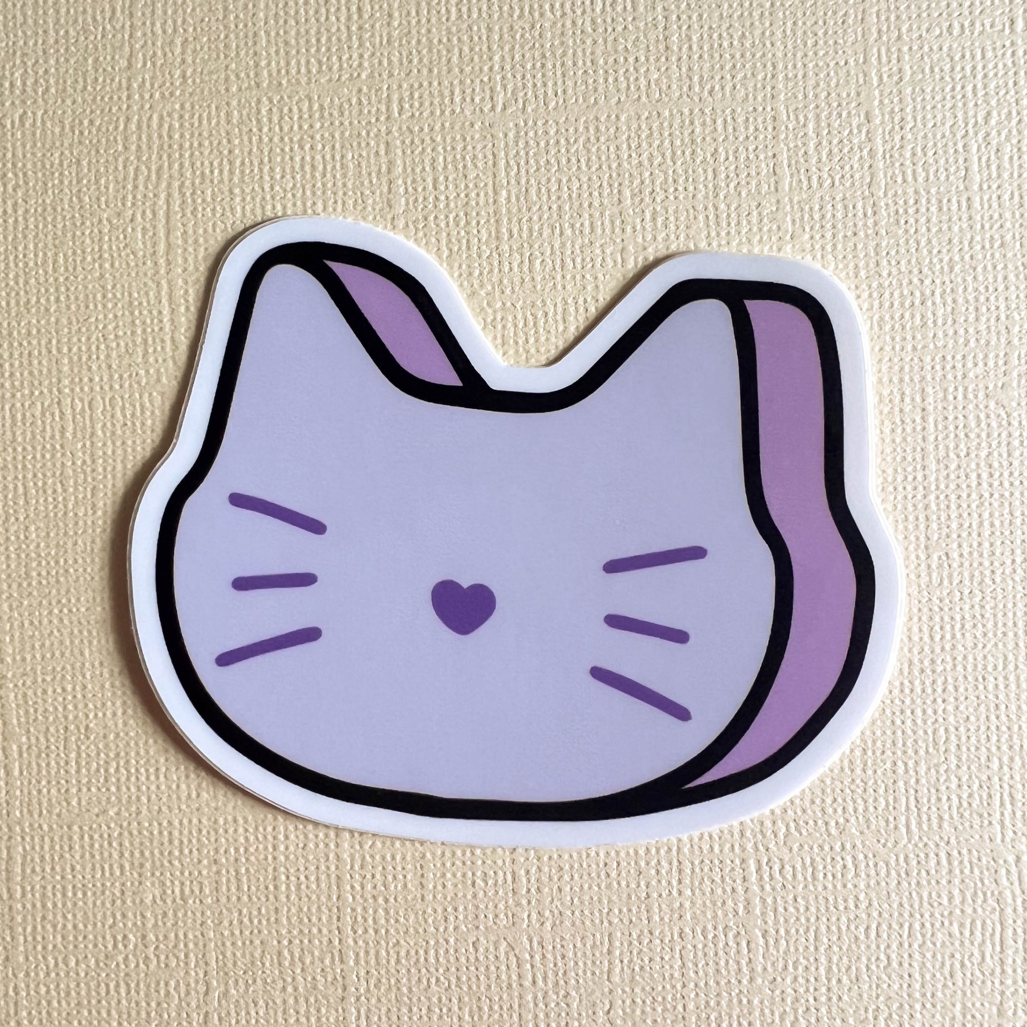 Sticker of a marshmallow cat face with a purple heart on a yellow background