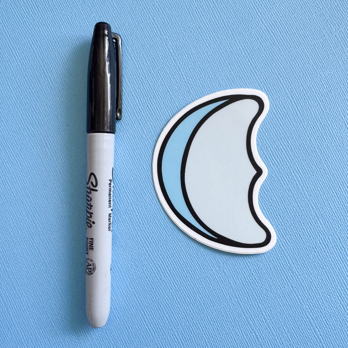 Moon-shaped marshmallow sticker next to a Sharpie on a blue background