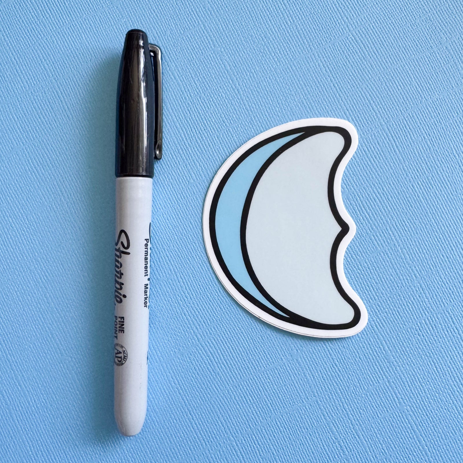 Moon-shaped marshmallow sticker next to a Sharpie on a blue background