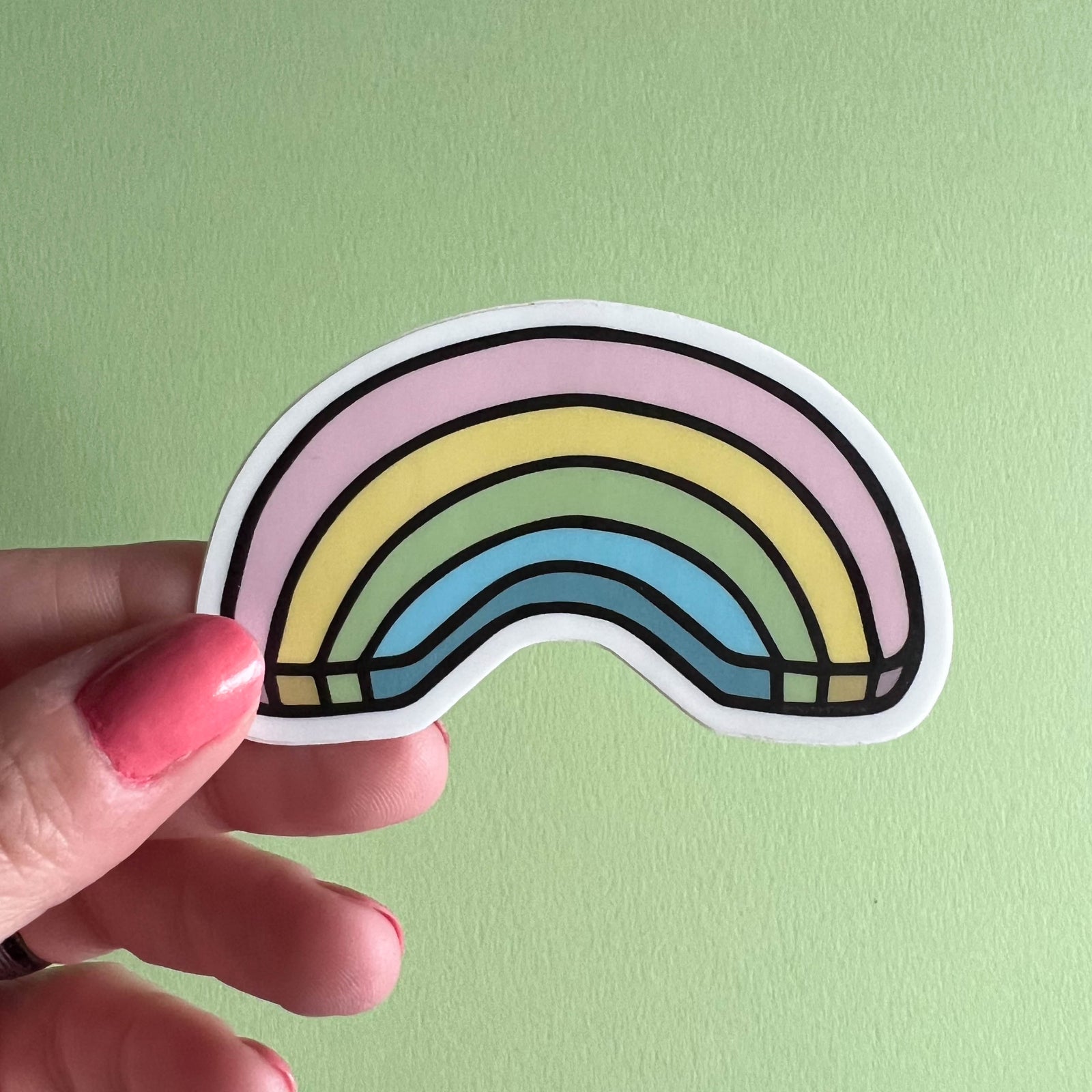 Hand holding a rainbow-shaped sticker against a light green background