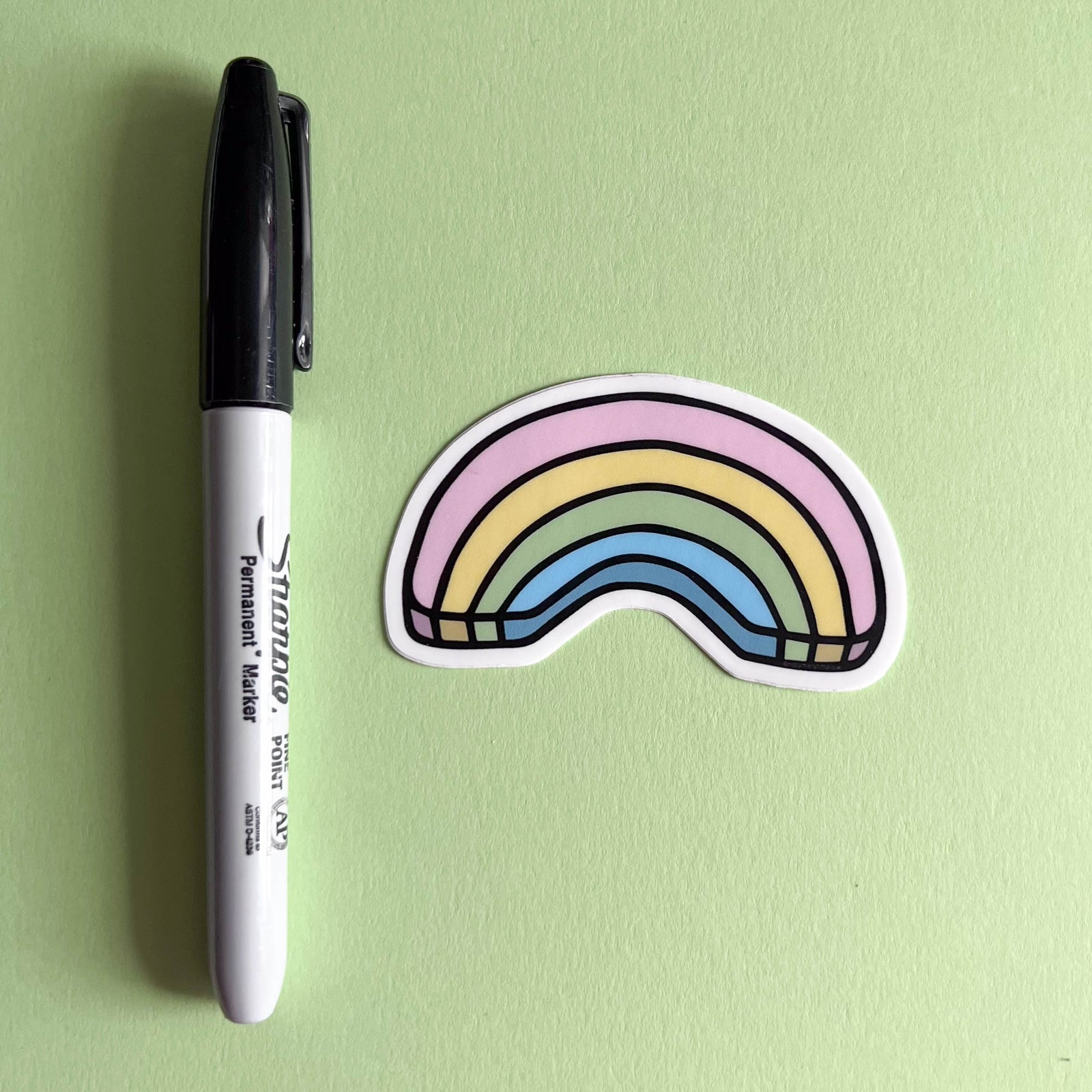 Black permanent marker next to a colorful rainbow sticker on a green background