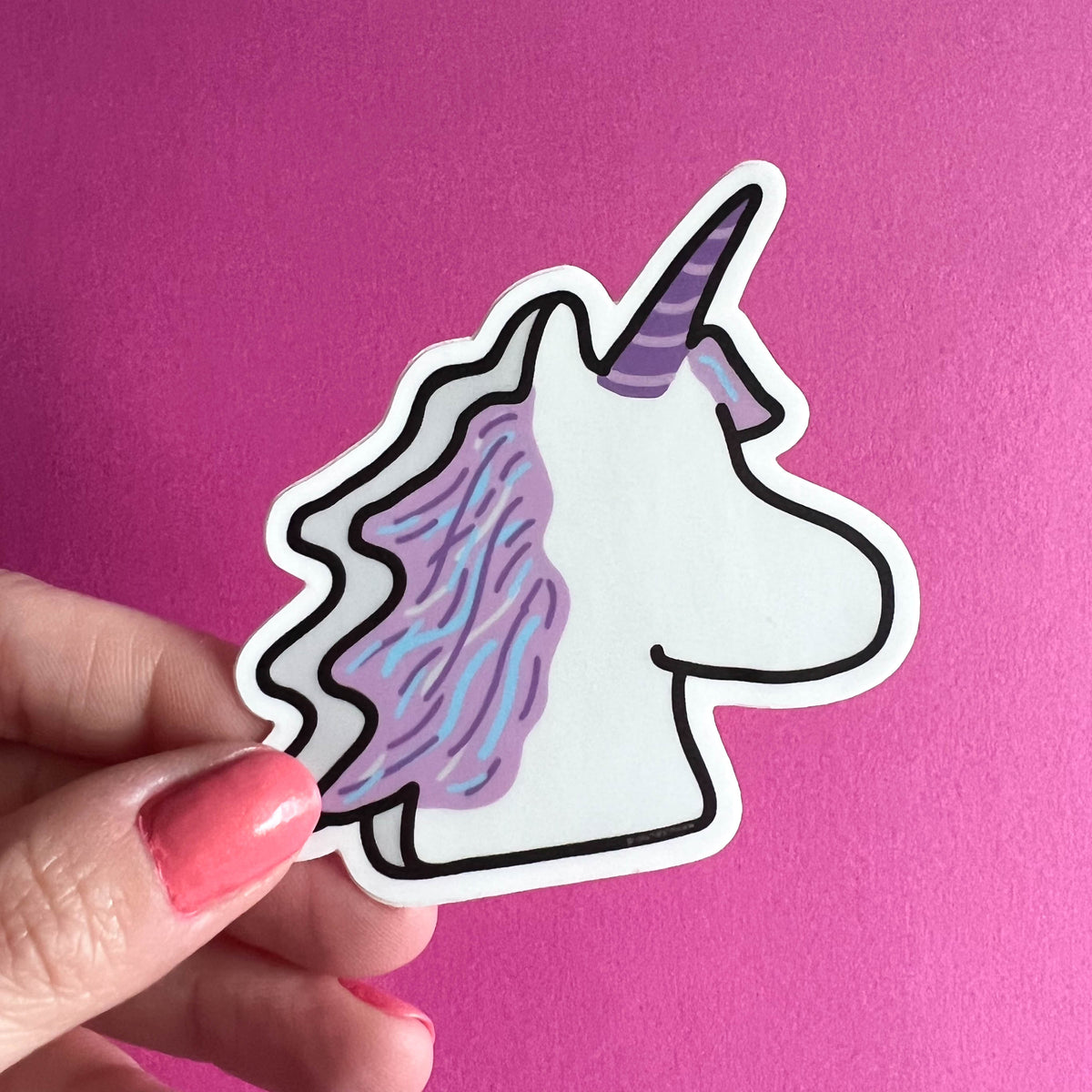 Hand holding a marshmallow unicorn sticker with a colorful horn against a pink background