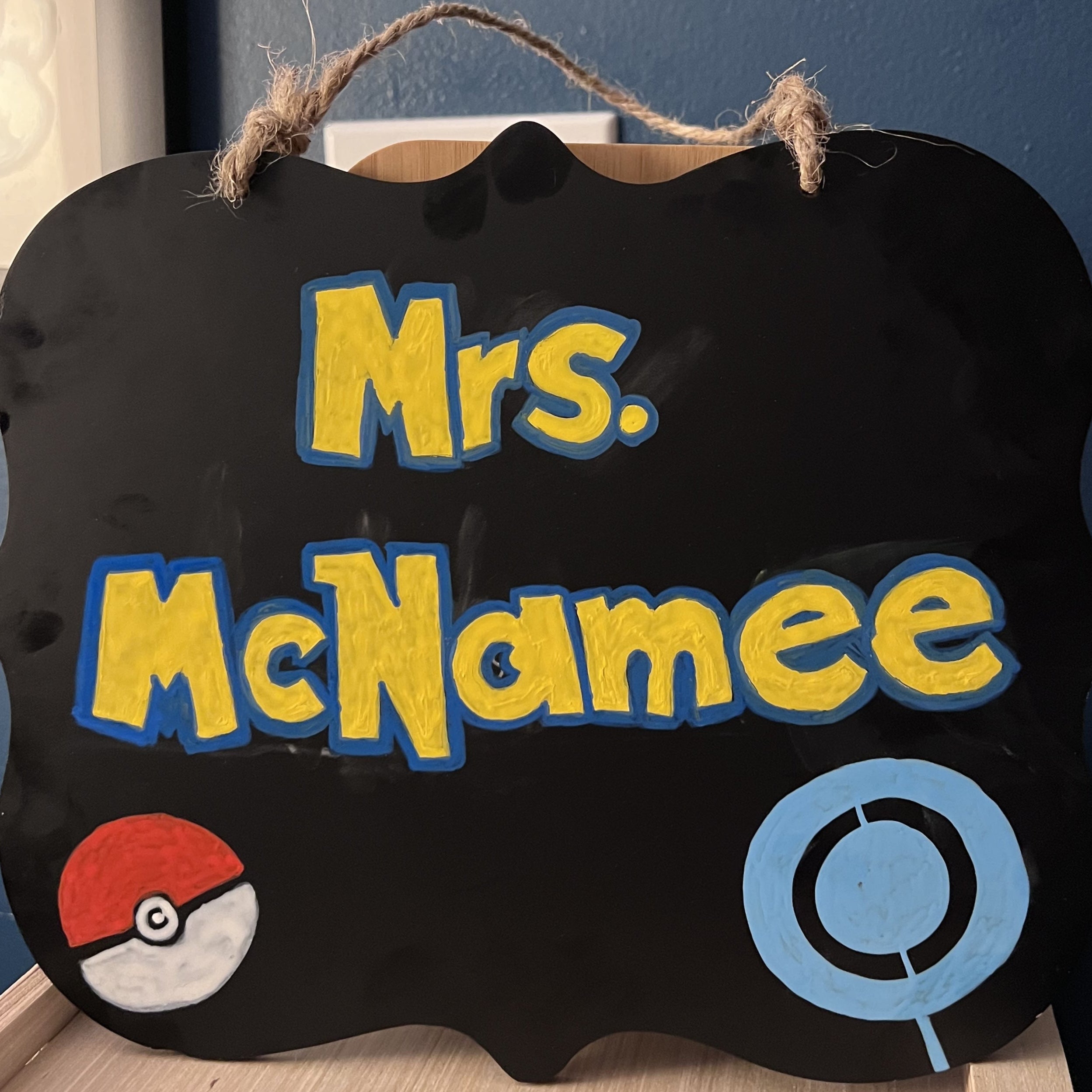 Decorative sign with 'Mrs. McNamee' Pokemon-inspired hand lettering text and logos on a black background