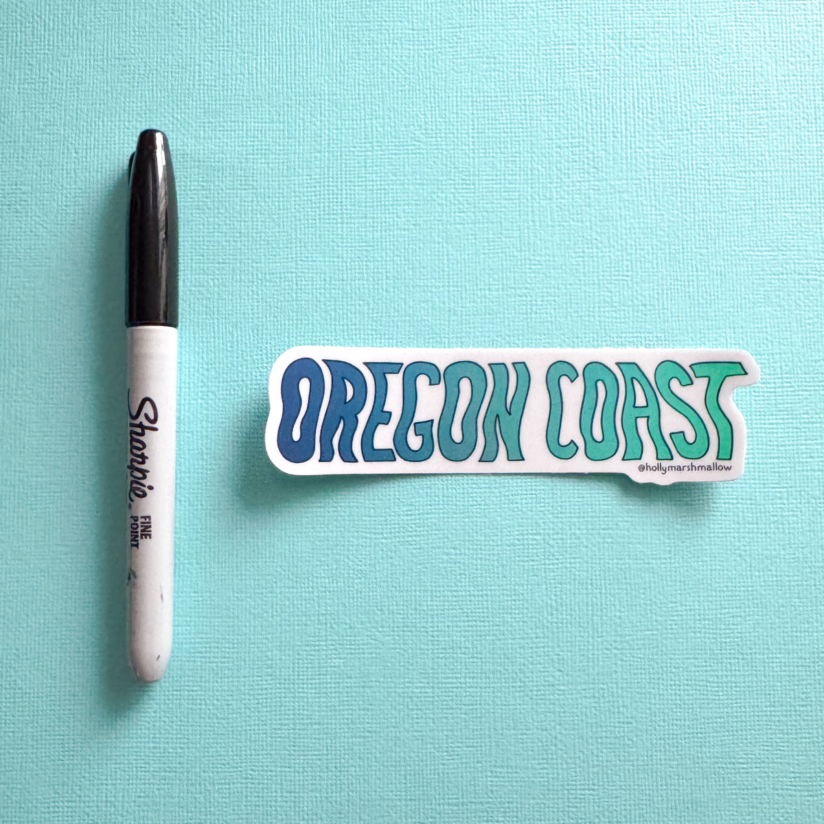 Sticker with 'OREGON COAST' text next to a Sharpie marker on a light blue background