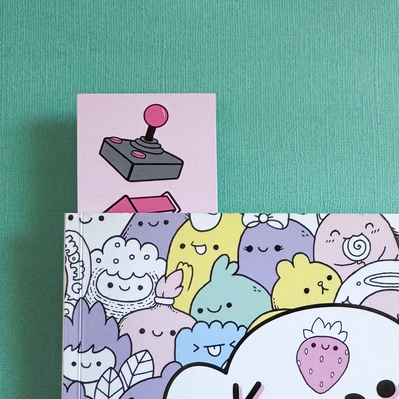 Bookmark with a joystick on the front peeking out of a book with kawaii characters on the front