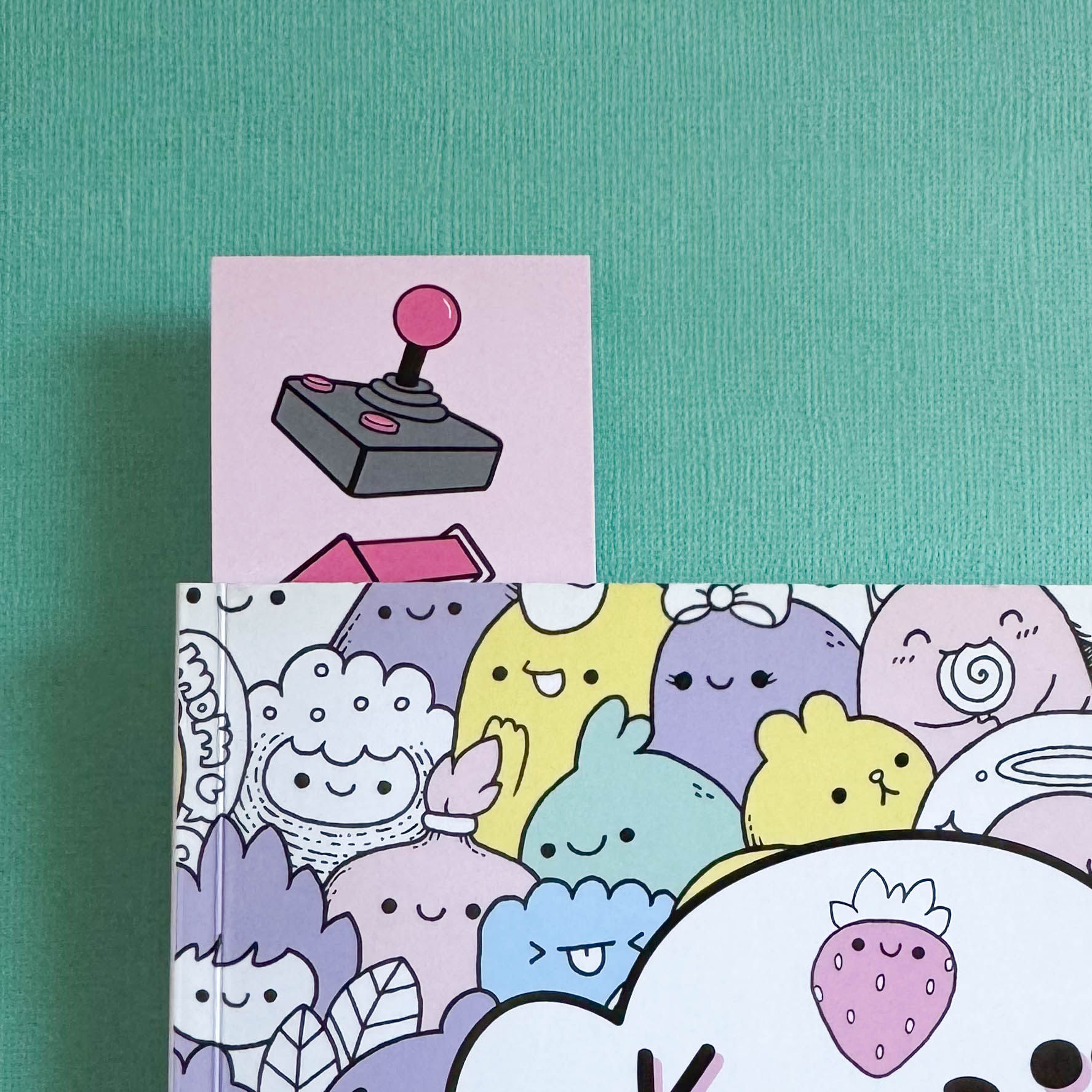 Bookmark with a joystick on the front peeking out of a book with kawaii characters on the front