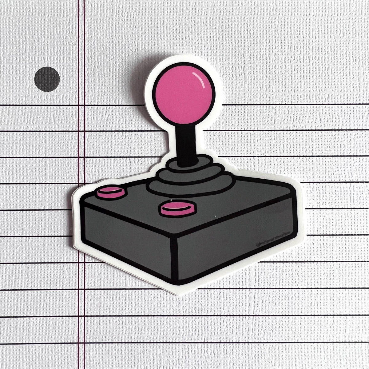 Joystick sticker with pink top and buttons on a lined paper background
