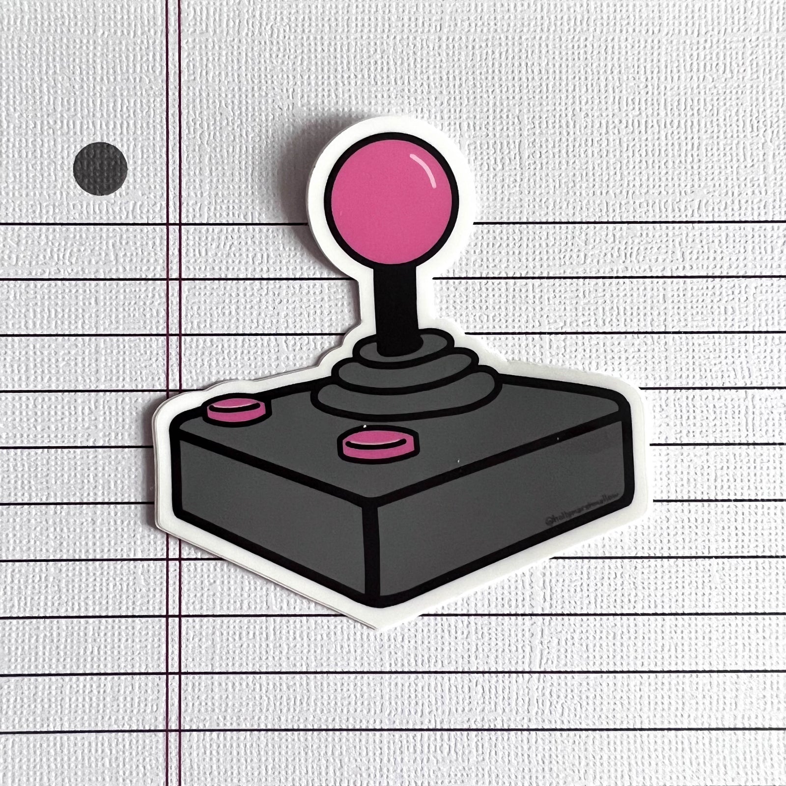 Joystick sticker with pink top and buttons on a lined paper background