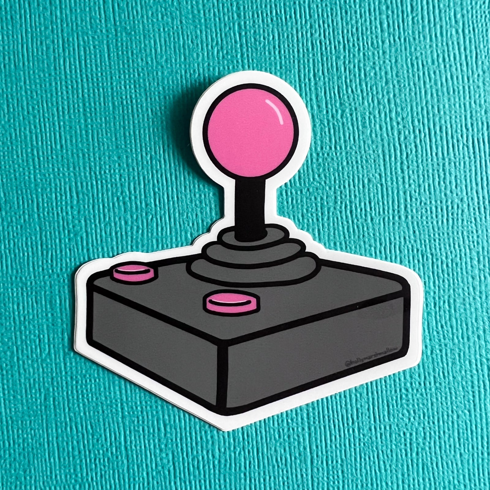 Joystick sticker with pink ball and buttons on a teal background