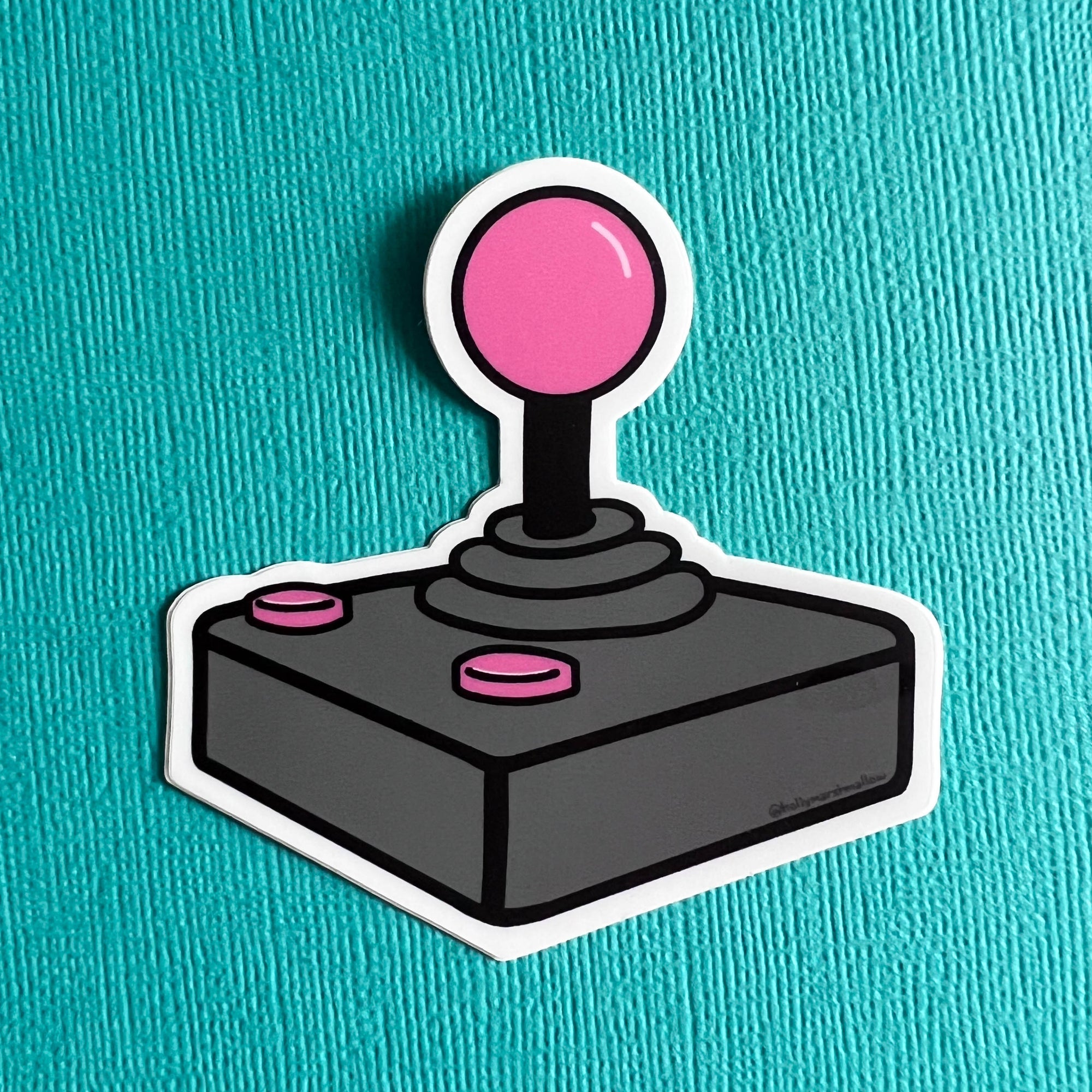 Joystick sticker with pink ball and buttons on a teal background