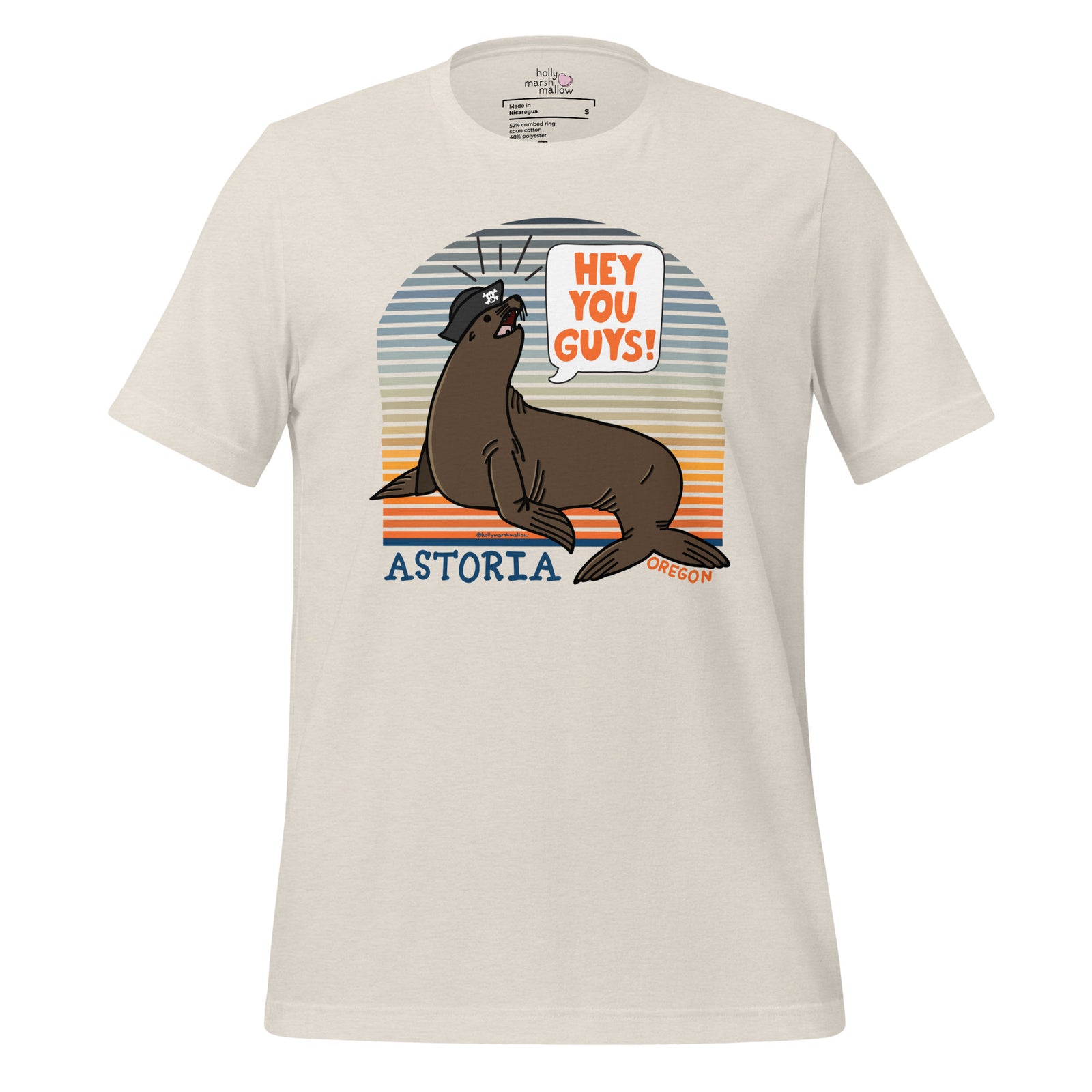 A Heather Dust t-shirt on a white background. The t-shirt has a sea lion in a tricorn hat yelling HEY YOU GUYS with a sunset stripe background and hand-lettered Astoria, Oregon on the bottom