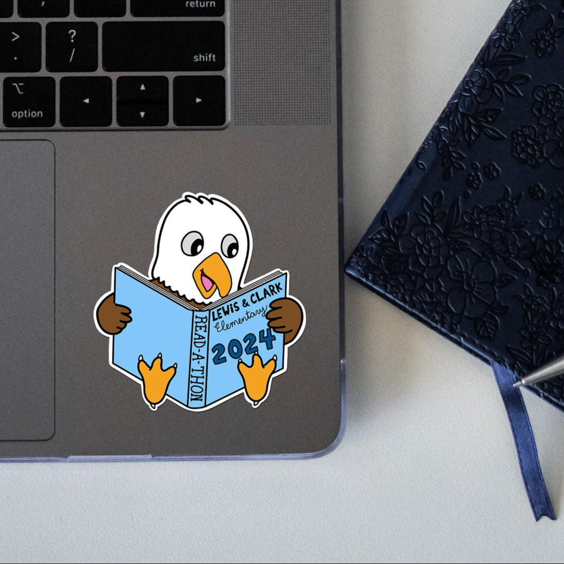 Laptop with a sticker of a bird reading a book, next to a notebook and pen on a white surface.