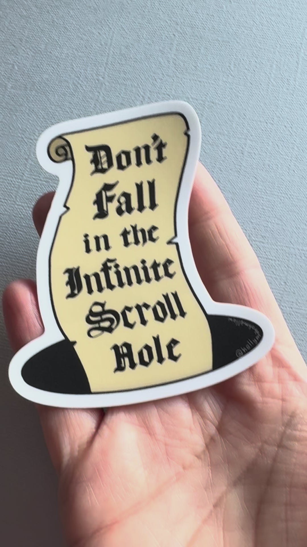 video of a hand holding a sticker of an illustrated parchment scroll in a hole with the hand lettered words Don't Fall in the Infinite Scroll Hole