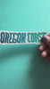 Video of a hand holding a Sticker with hand-lettered 'OREGON COAST' text on a teal background