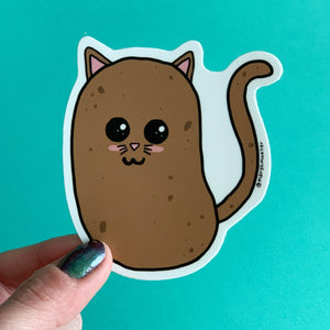 Hand holding Potato Cat Die Cut Sticker on a teal background